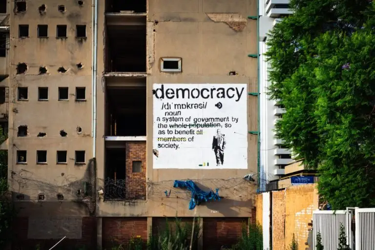 An abandoned building features a prominent democracy poster amidst urban decay.